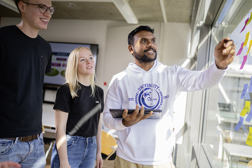 Eine Gruppe BWL-Studierender steht an einem Fenster mit Post-Its