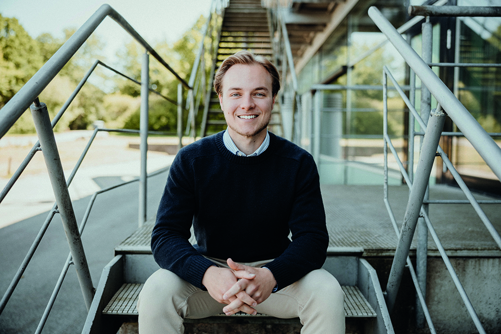 Testimonial Wirtschaftspsychologie Studium an der FH Westküste: Ein junger Mann sitzt auf einer Treppe und lächelt in die Kamera