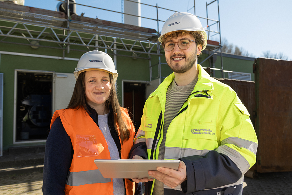 Mitarbeitende der Stadtwerke Norderstedt stehen mit Helm vor Baustelle
